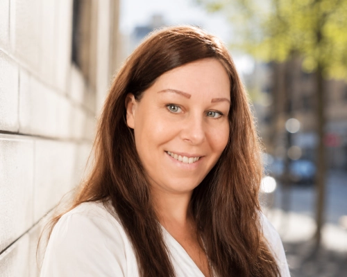 Porträtt av Jenny Månsson, erfaren expert inom SEO, GEO och AI-sök. En solig dag utomhus i stadsmiljö med grönska syns i bakgrunden.